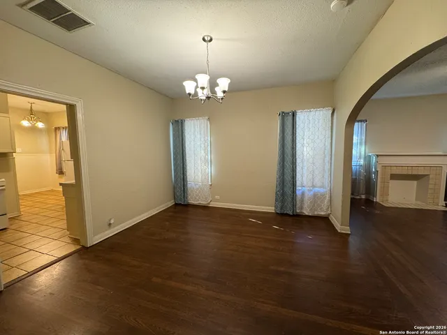 an empty room with wooden floor chandelier and windows