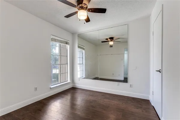 an empty room with wooden floor fan and windows