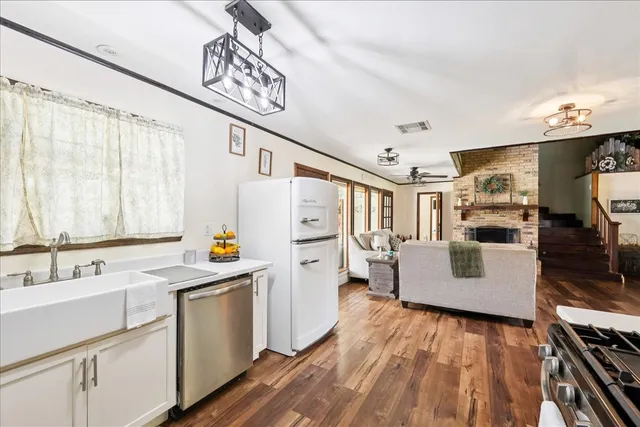 a kitchen with stainless steel appliances a refrigerator a sink dishwasher and white cabinets with wooden floor