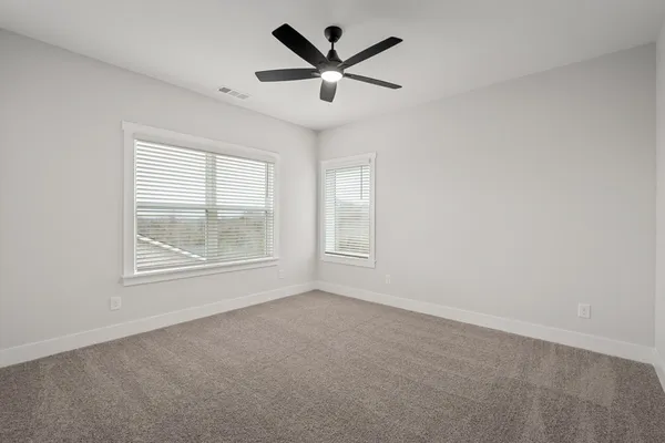 an empty room with ceiling fan and windows