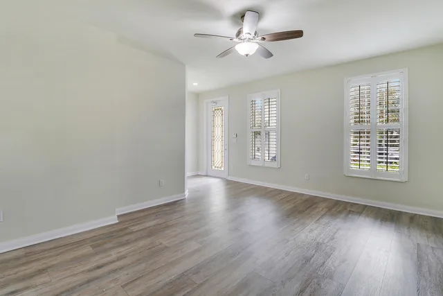 an empty room with wooden floor chandelier fan and windows