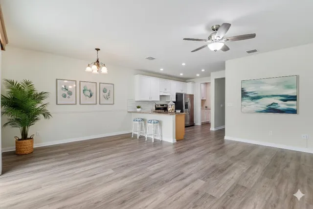 a view of an empty room and kitchen with wooden floor