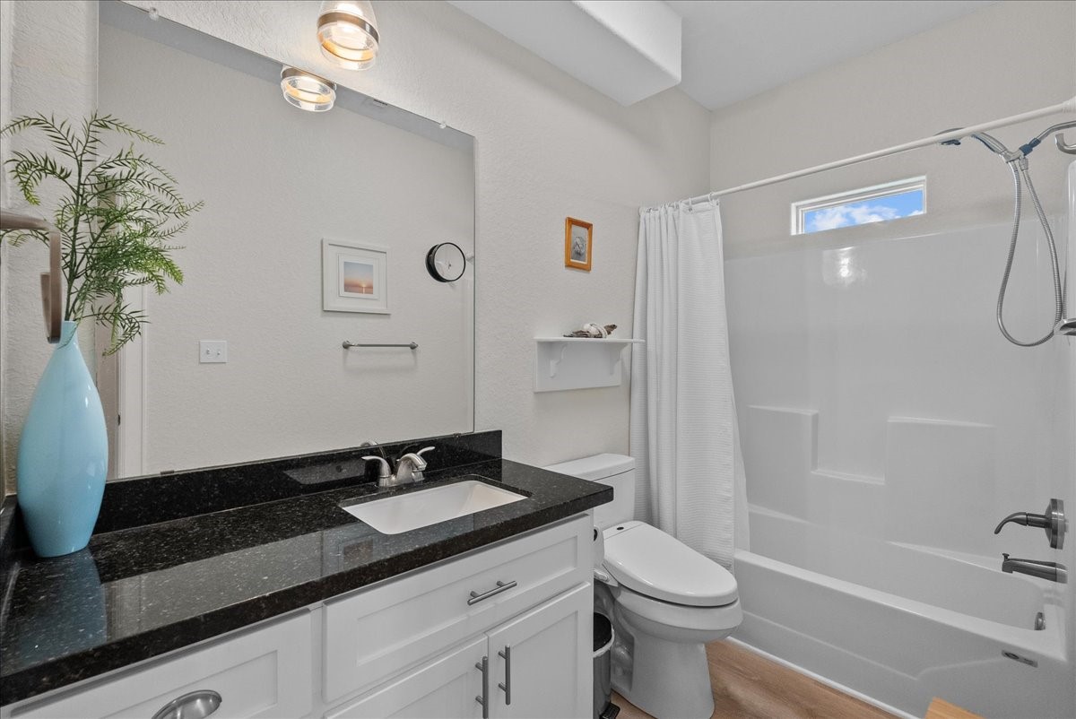 130 Beachcomber Avenue Surfside Beach, TX 77541 - Photo 16 of 33 This bathroom features a modern design with a sleek granite countertop, white cabinetry, and a stylish light fixture. It includes a bathtub with a shower, a large mirror, and a small window for natural light. A decorative vase and wall art add a touch of elegance.