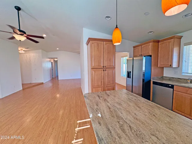 a kitchen with stainless steel appliances granite countertop a refrigerator a sink dishwasher a stove and white countertops with wooden floor