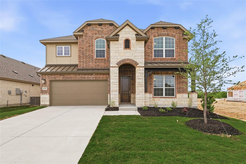 Brick and stone facade featuring an arched entry, two-car garage, and metal roof accents