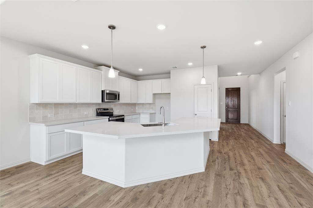 3737 Pitchfork Terrace Anna, TX 75409 - Photo 8 of 33 Modern kitchen featuring a large central island with a sink, white cabinetry, integrated stainless steel appliances, and wood-finish flooring