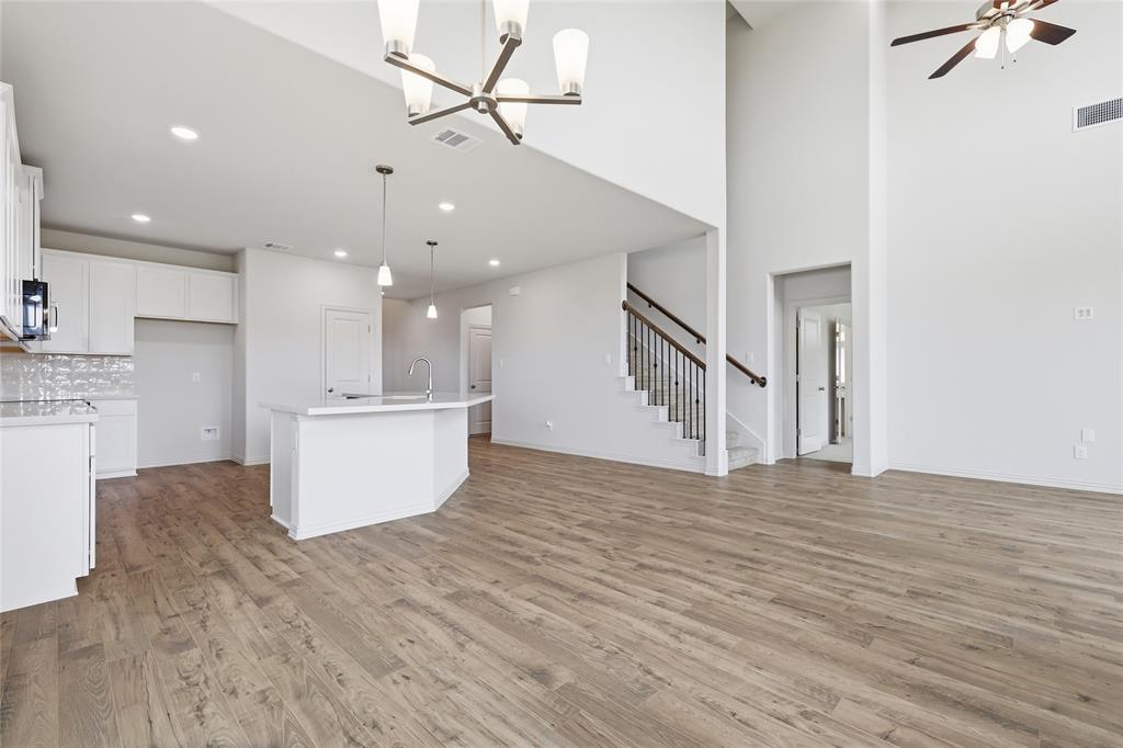 3737 Pitchfork Terrace Anna, TX 75409 - Photo 10 of 33 Open-concept living area featuring high ceilings, wood-finish flooring, a kitchen island with pendant lighting, white cabinetry, and a staircase with wrought iron balusters