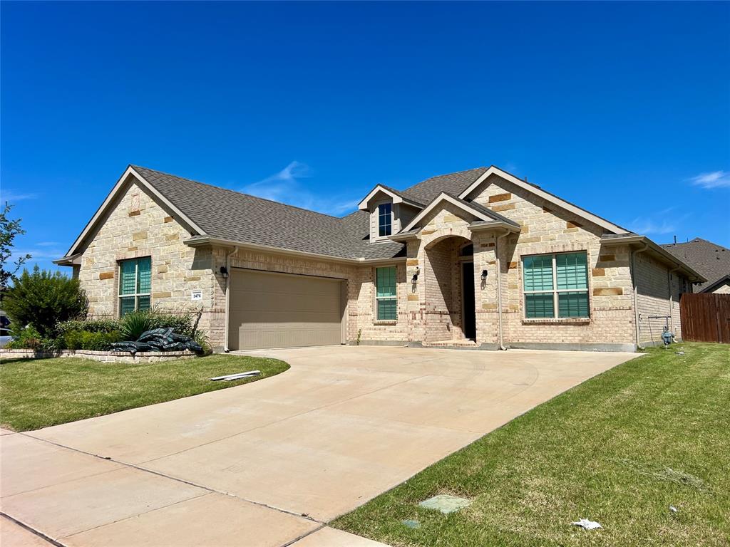 French country inspired facade featuring a shingled roof, a front yard, concrete driveway, and brick siding
