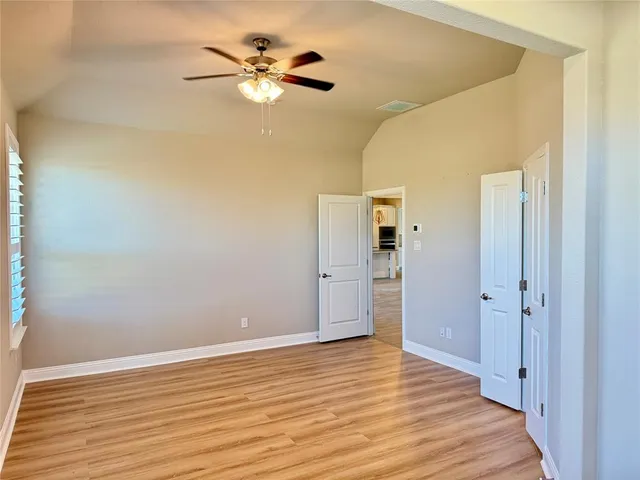 a view of an empty room with chandelier fan and wooden floor