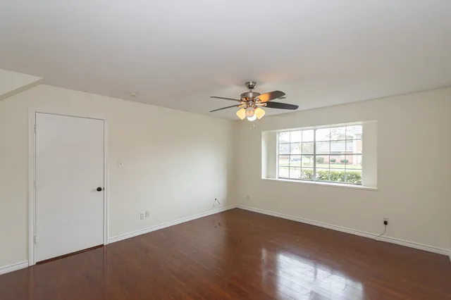 an empty room with wooden floor chandelier fan and windows