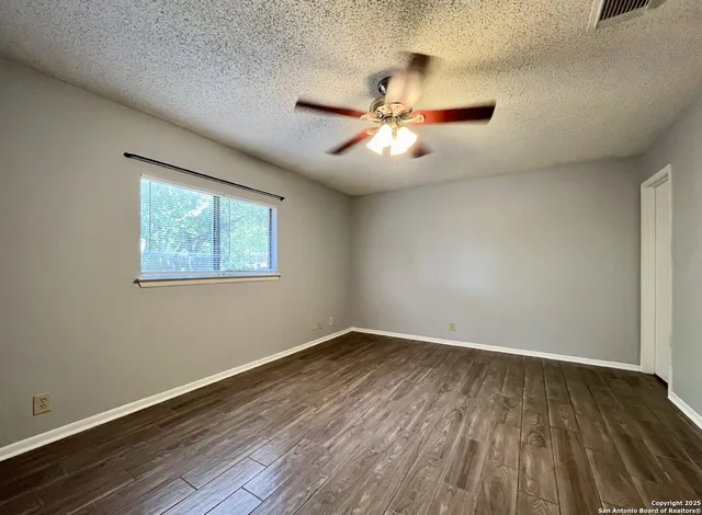 a view of empty room with wooden floor and fan