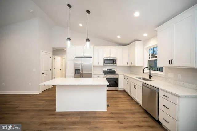 a large kitchen with stainless steel appliances kitchen island a large counter top a stove a sink cabinets and a wooden floor