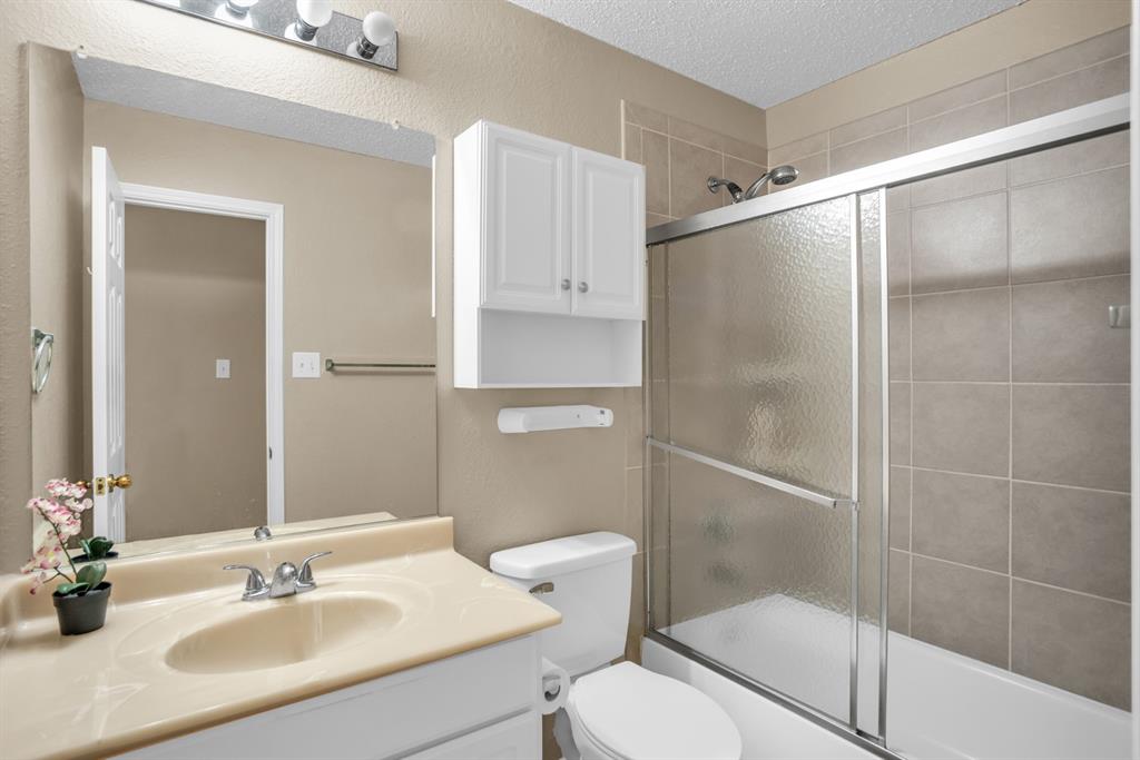 8308 Spring Ridge Drive Plano, TX 75025 - Photo 18 of 28 Full bathroom featuring a single vanity with an integrated sink, a large wall-mounted mirror, overhead vanity lighting, a built-in wall cabinet, and a combination tub and shower with a sliding glass door and tile surround