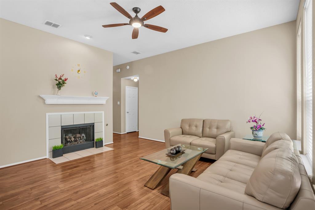 8308 Spring Ridge Drive Plano, TX 75025 - Photo 5 of 28 Spacious living area featuring high ceilings, wood-finish flooring, a fireplace with a white mantel, and a ceiling fan