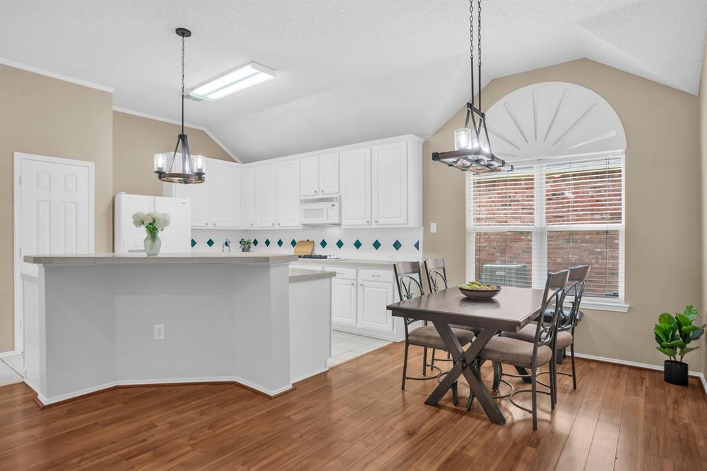 8308 Spring Ridge Drive Plano, TX 75025 - Photo 7 of 28 Spacious kitchen and dining area featuring white cabinetry, light countertops, wood-finish flooring, a vaulted ceiling, and an arched window with sunburst detailing