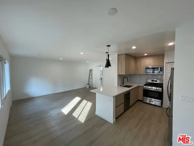 a living room with stainless steel appliances kitchen island hardwood floor and a sink
