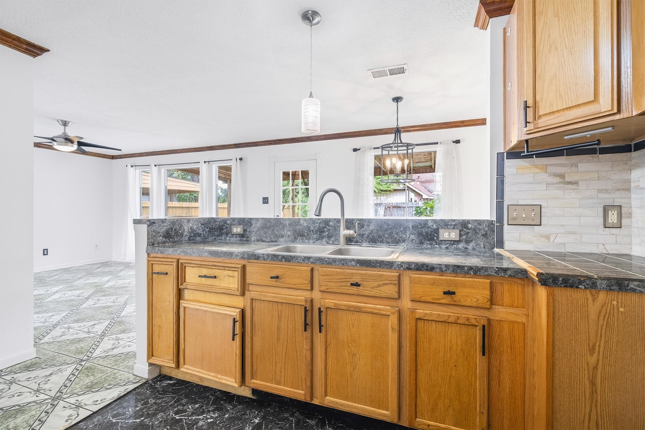 5426 Bourgeois Road Houston, TX 77066 - Photo 17 of 43 Spacious kitchen with a sleek black countertop, warm wood cabinetry, and a double sink, seamlessly flowing into a bright living area with large windows and a stylish ceiling fan.