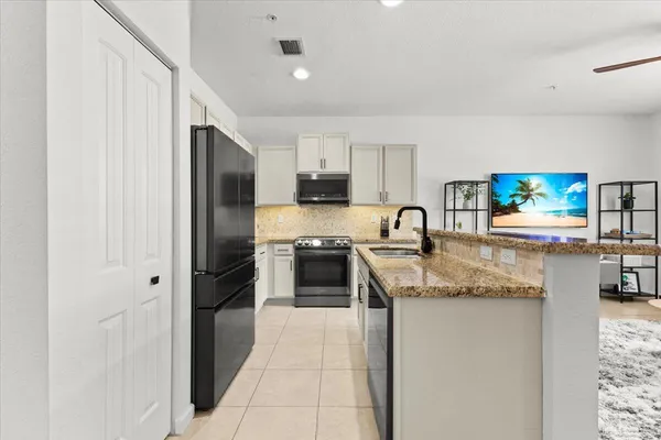 a kitchen with granite countertop a refrigerator a sink a stove a microwave a counter top space and cabinets