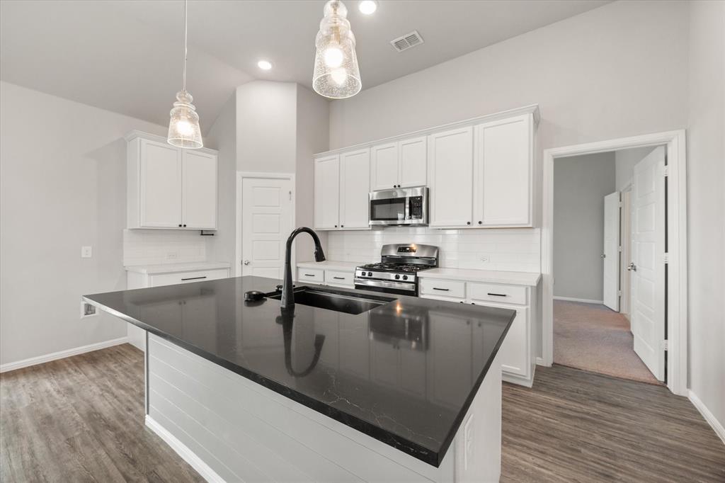 6910 Prairieside Trail Venus, TX 76084 - Photo 14 of 40 Kitchen featuring a large island with a dark countertop, farm sink, white cabinetry with black hardware, stainless steel appliances, and wood-look flooring.