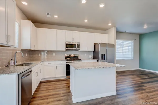 a kitchen with stainless steel appliances a stove top oven a sink a refrigerator white cabinets and wooden floor