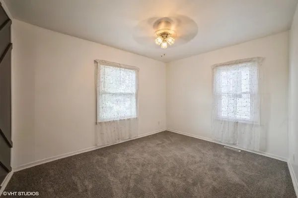 an empty room with a chandelier fan and windows
