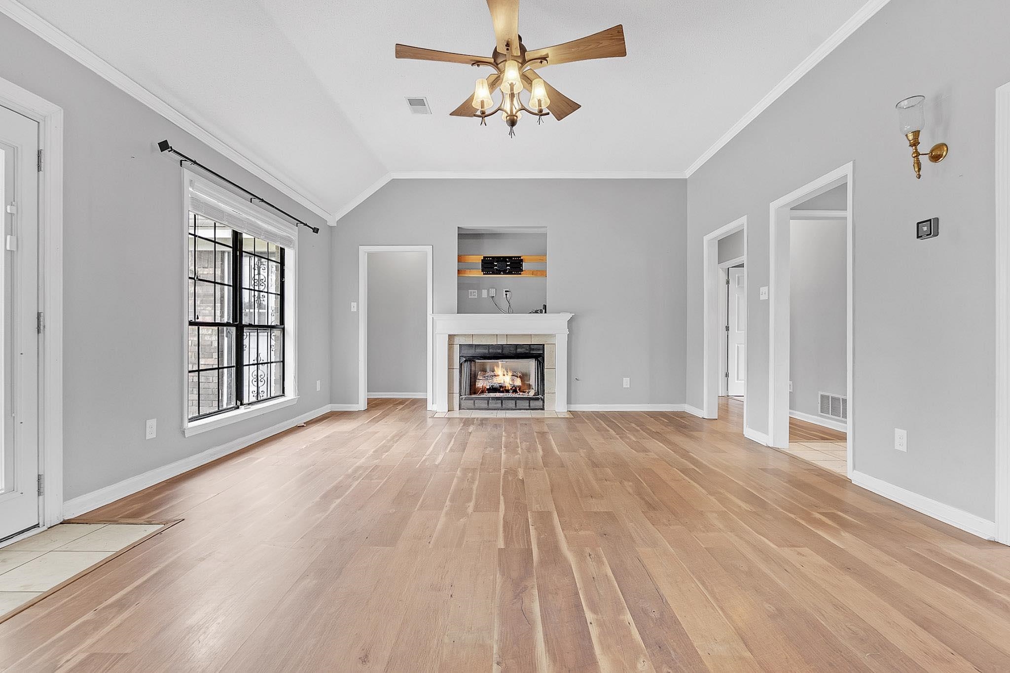 4788 Shadow View Lane Bartlett, TN 38002 - Photo 8 of 33 Unfurnished living room with light wood-style flooring, a ceiling fan, a tiled fireplace, baseboards, and crown molding