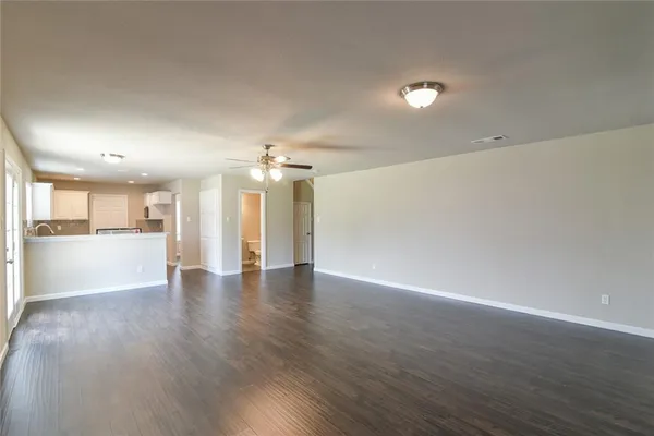 a view of an empty room with wooden floor and a kitchen