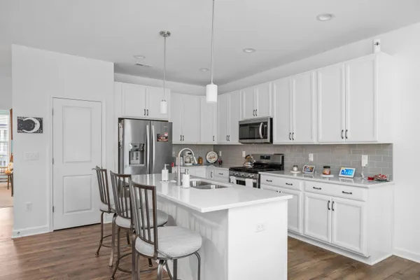 a kitchen with stainless steel appliances a microwave a stove a sink dishwasher a refrigerator white cabinets and wooden floor