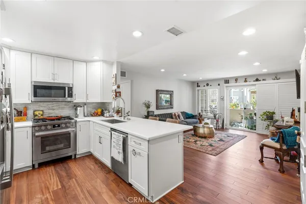 a large white kitchen with wooden floor and stainless steel appliances