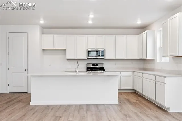 a kitchen with stainless steel appliances granite countertop a stove top oven a sink and white cabinets