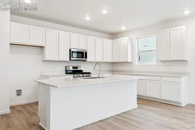 a kitchen with stainless steel appliances granite countertop a stove top oven a sink a refrigerator white cabinets and wooden floor