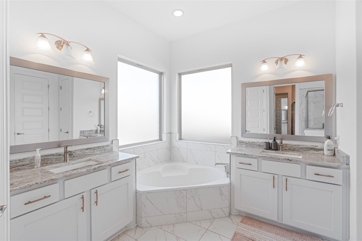 3037 Sage Ranch Drive Leander, TX 78641 - Photo 16 of 26 a bathroom with a granite countertop double vanity sink a mirror and a bathtub