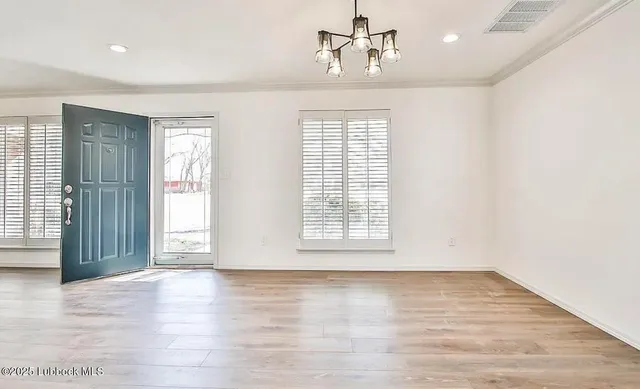 an empty room with wooden floor chandelier and windows