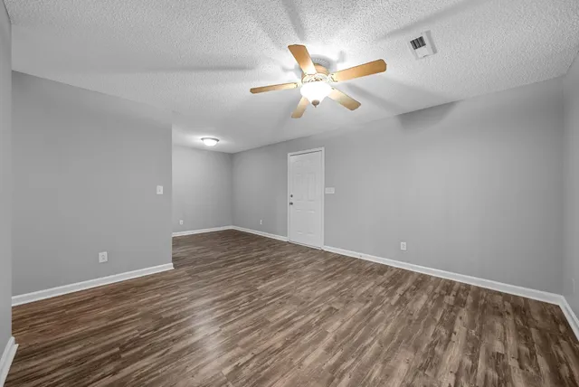a view of an empty room with wooden floor and a ceiling fan
