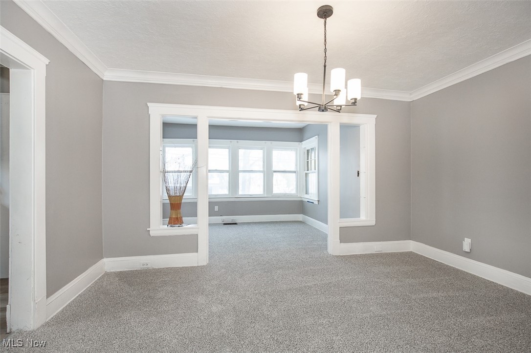 1045 Carlyon Road Cleveland, OH 44112 - Photo 7 of 26 Unfurnished room with crown molding, a chandelier, light colored carpet, and a textured ceiling