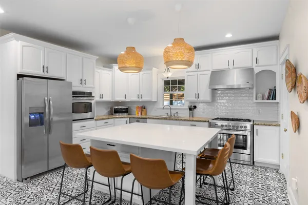 a kitchen with stainless steel appliances a dining table chairs refrigerator and sink