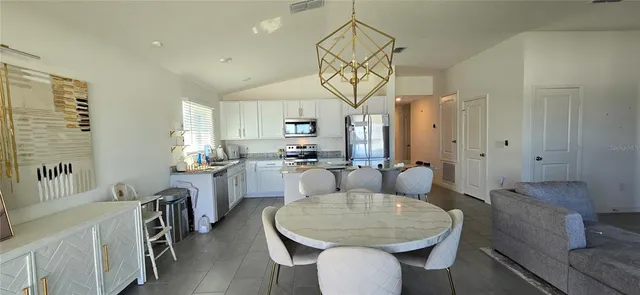 a living room with stainless steel appliances furniture a dining table and a chandelier