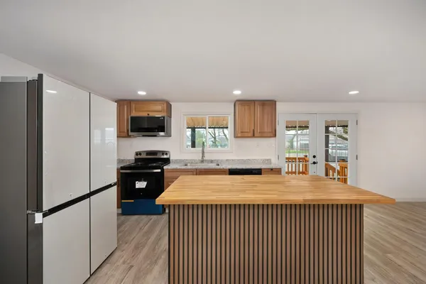 a kitchen with stainless steel appliances granite countertop a refrigerator oven a sink dishwasher and white cabinets with wooden floor