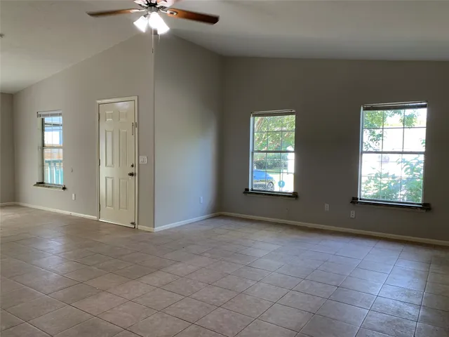 an empty room with chandelier fan and windows