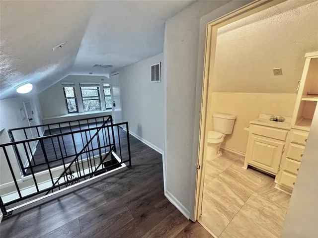 a view of a hallway with wooden floor and a bathroom