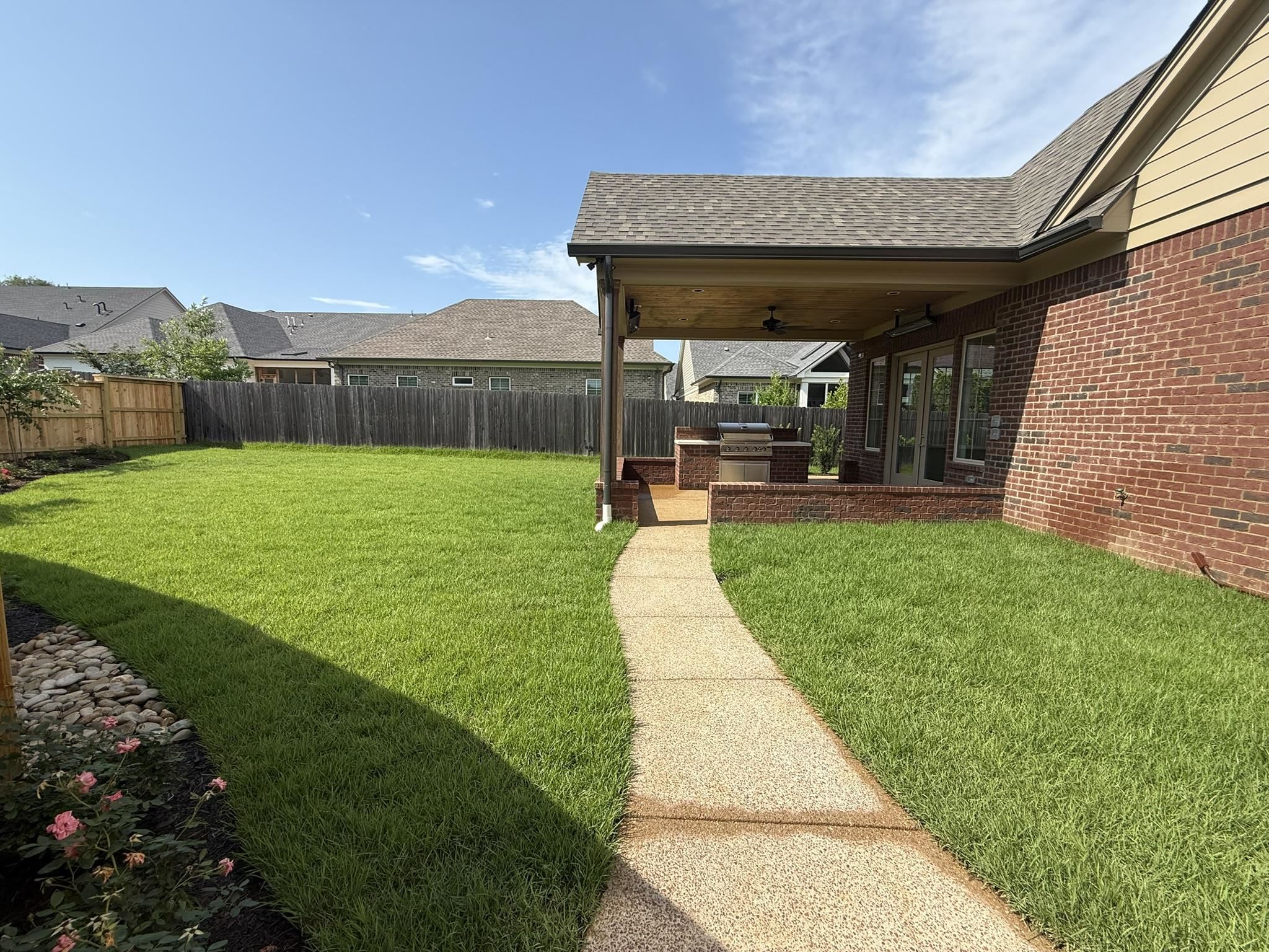 10132 Rokeby Farm Lane Collierville, TN 38017 - Photo 22 of 24 Expansive backyard featuring a covered patio, built-in outdoor kitchen, brick exterior, and a manicured lawn with a concrete pathway