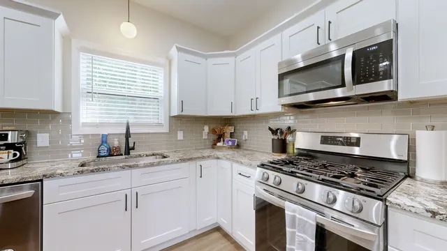 a kitchen with stainless steel appliances white cabinets granite counter tops and a window