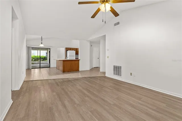 an empty room with wooden floor chandelier fan and windows