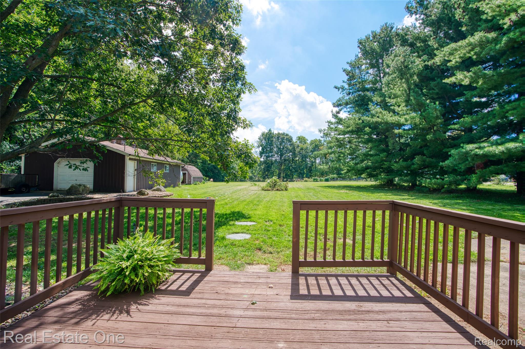 5130 Iosco Road Webberville, MI 48892 - Photo 8 of 39 Expansive backyard featuring a manicured lawn, mature trees, and an elevated wood deck with railings