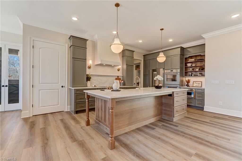 6806 Brennan Way Oak Ridge, NC 27310 - Photo 3 of 50 warm, welcoming and open kitchen with gorgeous custom cabinetry, large island with quartz countertops, induction stovetop, built ins and plenty of cabinetry