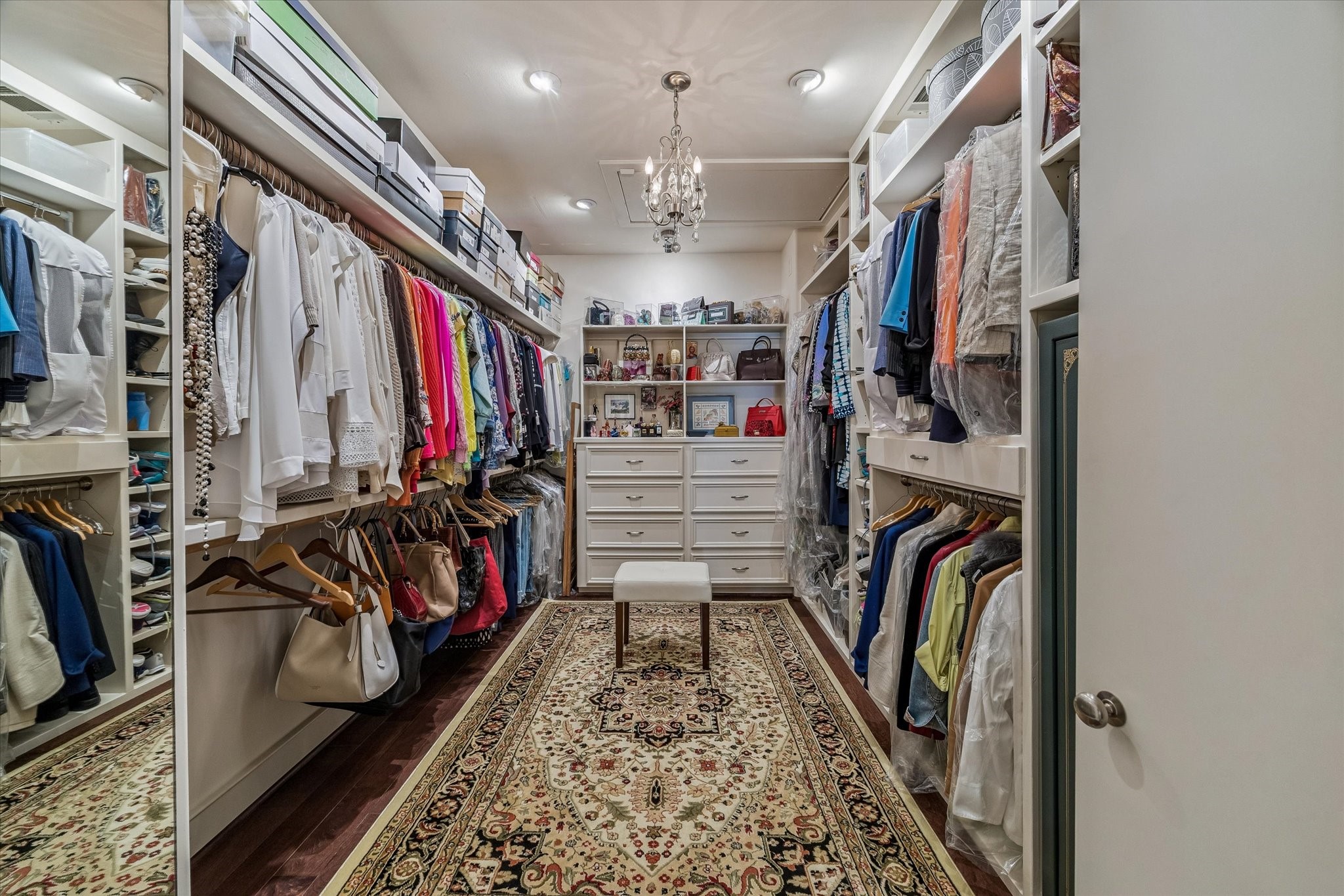 2415 West Main Street Houston, TX 77098 - Photo 37 of 48 Expansive primary closet with engineered hardwoods, built in cabinetry and drawers, dressing mirror, elegant chandelier, and soft recessed lighting, plus direct access to a floored attic.