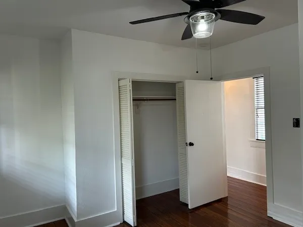 an empty room with wooden floor closet and fan
