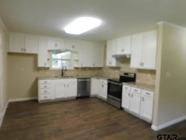 a kitchen with stainless steel appliances white cabinets a sink a stove a refrigerator and white cabinets