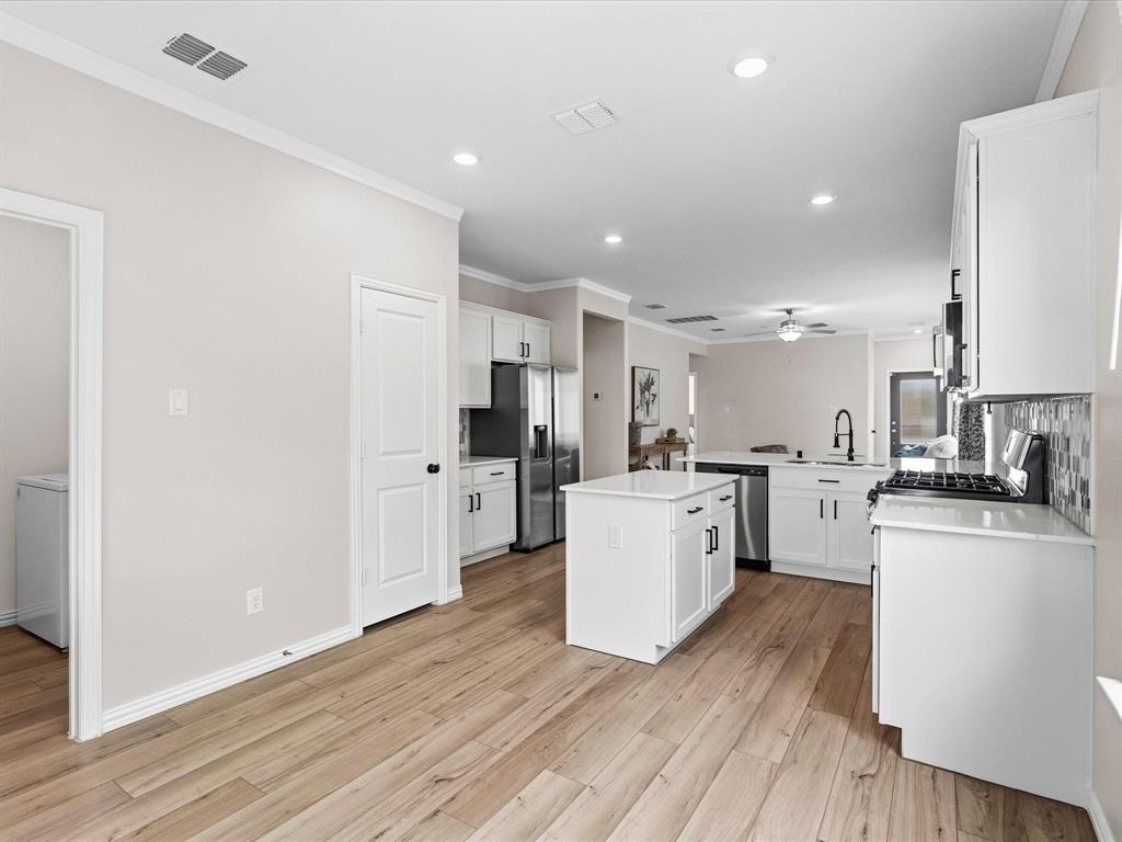 16936 Post Cedar Drive Justin, TX 76247 - Photo 9 of 30 Bright kitchen featuring a central island, white cabinetry, dark hardware, stainless steel appliances, and wood-finish flooring