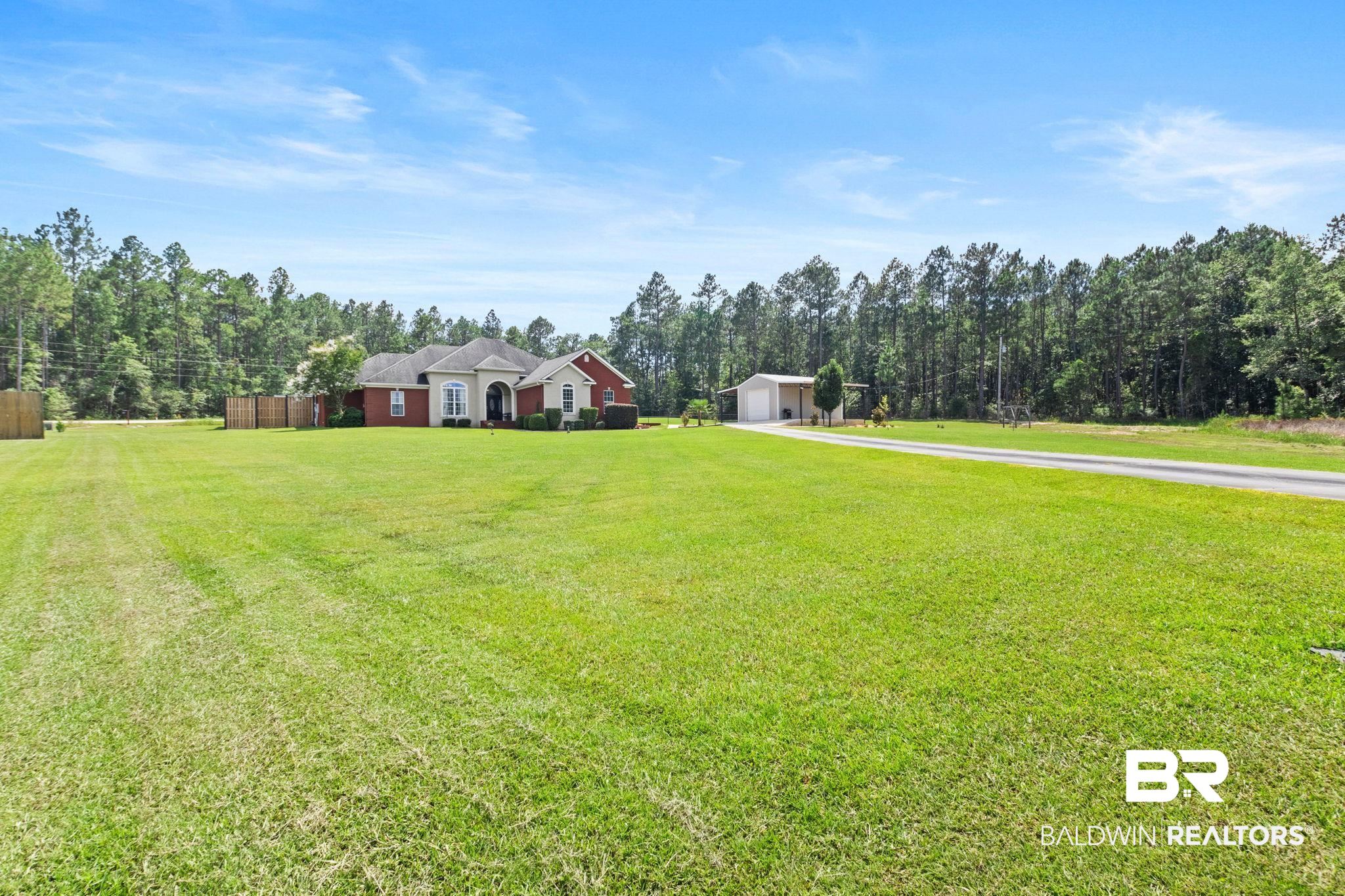 79 Whitetail Run Chatom, AL 36518 - Photo 11 of 82 Spacious property featuring a brick and stucco exterior residence, an extensive green lawn, a paved driveway, and a detached outbuilding
